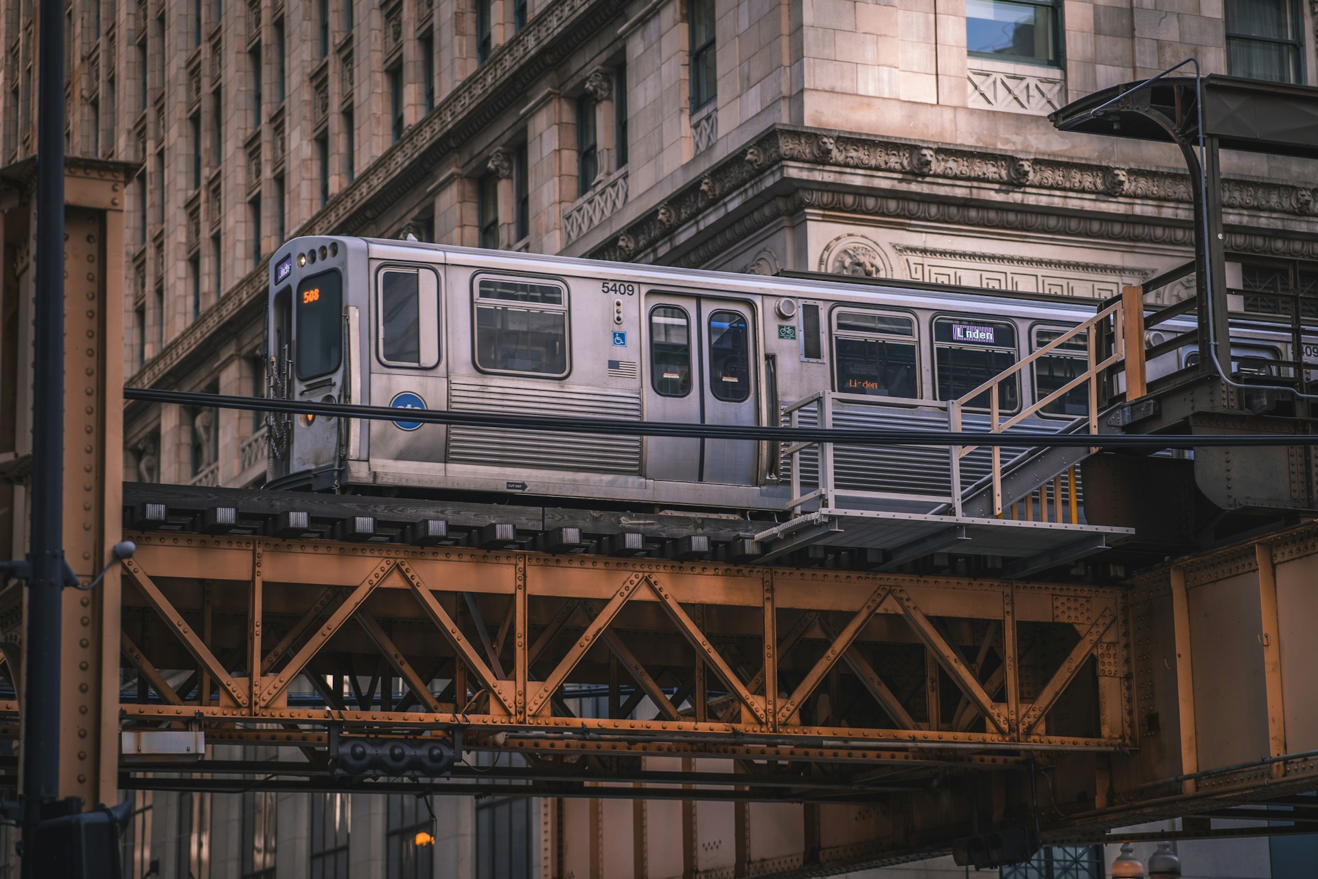 A photo of a CTA Purple Line train on elevated tracks in front of a stone building.